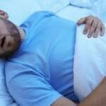 Man sleeping on bed with mouth open, possibly snoring